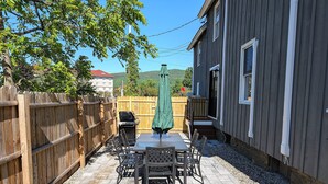 A patio with a table and chairs, a grill, and a wooden fence. - Village Overlook: Spacious 5 BR + Prime Location (Lake George)