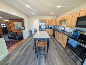 A modern kitchen with wooden cabinets, a central island, stainless steel appliances, and a dining area with a rug.