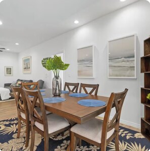 A dining area with a wooden table, six chairs, and a vase with green leaves. - Kona Charmer: Ocean View, Arcade Room (Kailua-Kona)