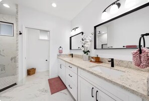 A modern bathroom with white marble floors, a large sink with a mirror, and a small plant on the counter. - Kona Charmer: Ocean View, Arcade Room (Kailua-Kona)