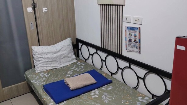 A single bed with a floral bedspread, a blue pillow, and a folded blanket. There is a wall-mounted artwork of a watermelon. - Mall of Asia - ASEANA Central (Pasay)