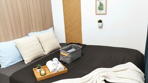 Ein ordentlich bezogenes Bett mit einer schwarzen Tagesdecke, einem weißen Handtuch und einem Tablett mit einer Pflanze und zusammengerollten Handtüchern.
