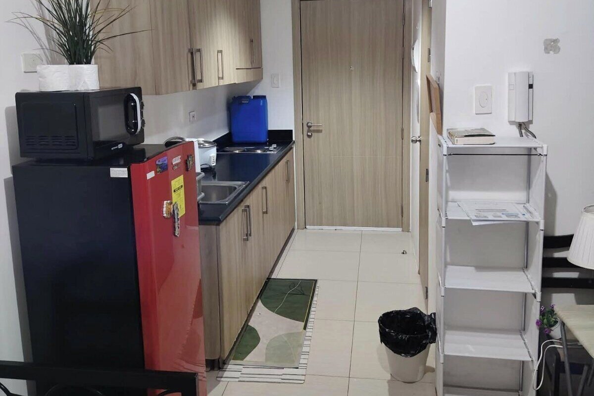Une cuisine compacte avec des meubles en bois, un réfrigérateur noir, un congélateur rouge, un four à micro-ondes et un bac de rangement bleu.