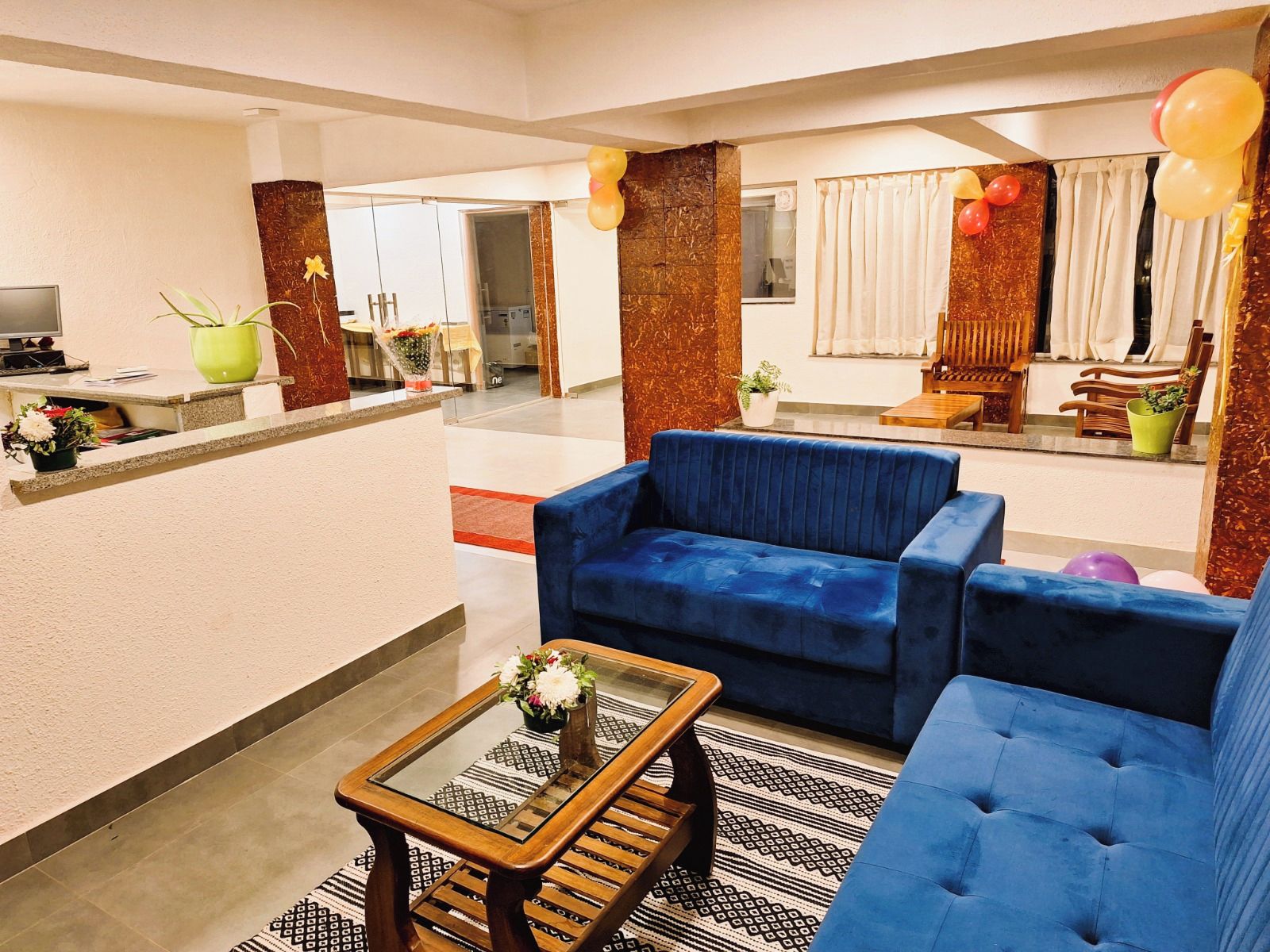 Eine moderne Hotellobby mit einem blauen Sofa, einem Glastisch und einem Empfangsbereich mit einer Zimmerpflanze.