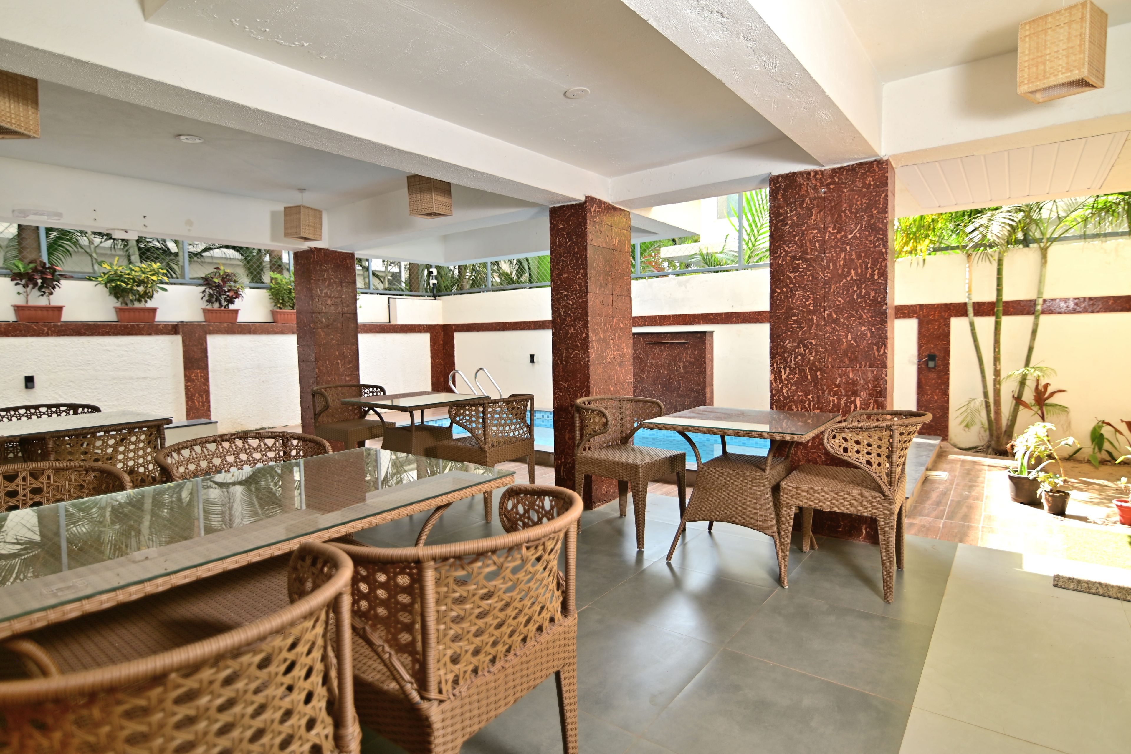 An indoor dining area with wicker furniture, a glass-top table, and a pool in the background.
