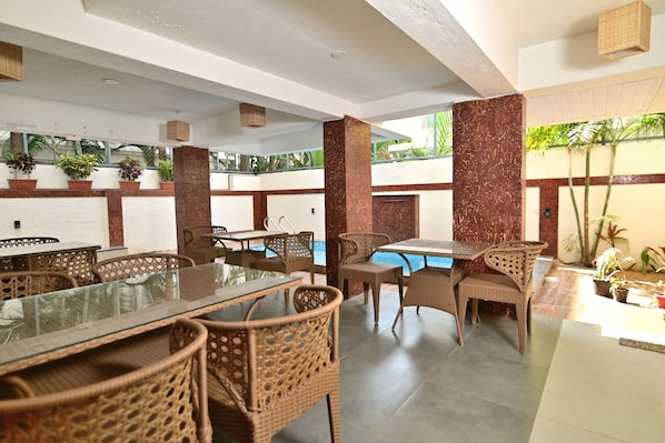 An indoor dining area with wicker furniture, a glass-top table, and a pool in the background.