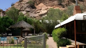 Un resort con piscina, una cabaña de techo de paja y montañas al fondo.