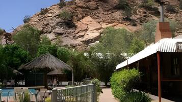 A resort with a pool, a thatched-roof hut, and a mountain backdrop.