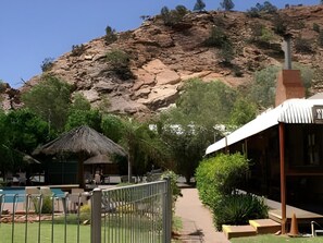 A resort with a pool, a thatched-roof hut, and a mountain backdrop.