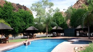 Piscina cercada por áreas de descanso, árvores e um cenário montanhoso.