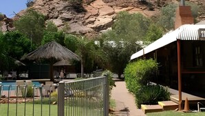 Resort com piscina, cabana de palha e montanhas ao fundo.