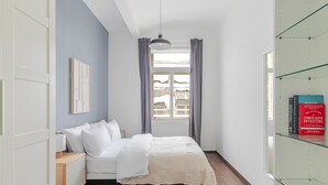 Une chambre à coucher avec un lit, une table de chevet, une fenêtre avec des rideaux et une bibliothèque remplie de livres.