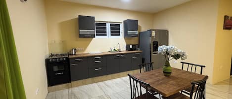 A modern kitchen with dark cabinets, a built-in oven, and a refrigerator. There is a dining table with chairs and a vase of flowers.