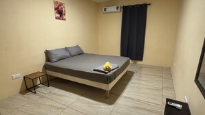 Ein Schlafzimmer mit Bett, kleinem Tisch, Klimaanlage und einem an der Wand montierten Fernseher.