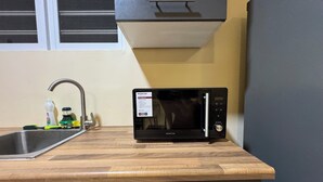 Eine Küche mit einer schwarzen Mikrowelle auf einer Holz Arbeitsplatte, einem Edelstahl-Spülbecken und einem Fenster darüber.