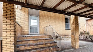 A brick exterior with a metal staircase leading to a door, a covered porch area, and a wooden deck. - Spacious 2BR Apt • Free Parking • Baden (Baden)