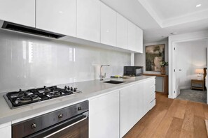 A modern kitchen with white cabinetry, a stainless steel stove, and a microwave. - Modern 2BR Southbank | City Views + 2 Balconies (Southbank)