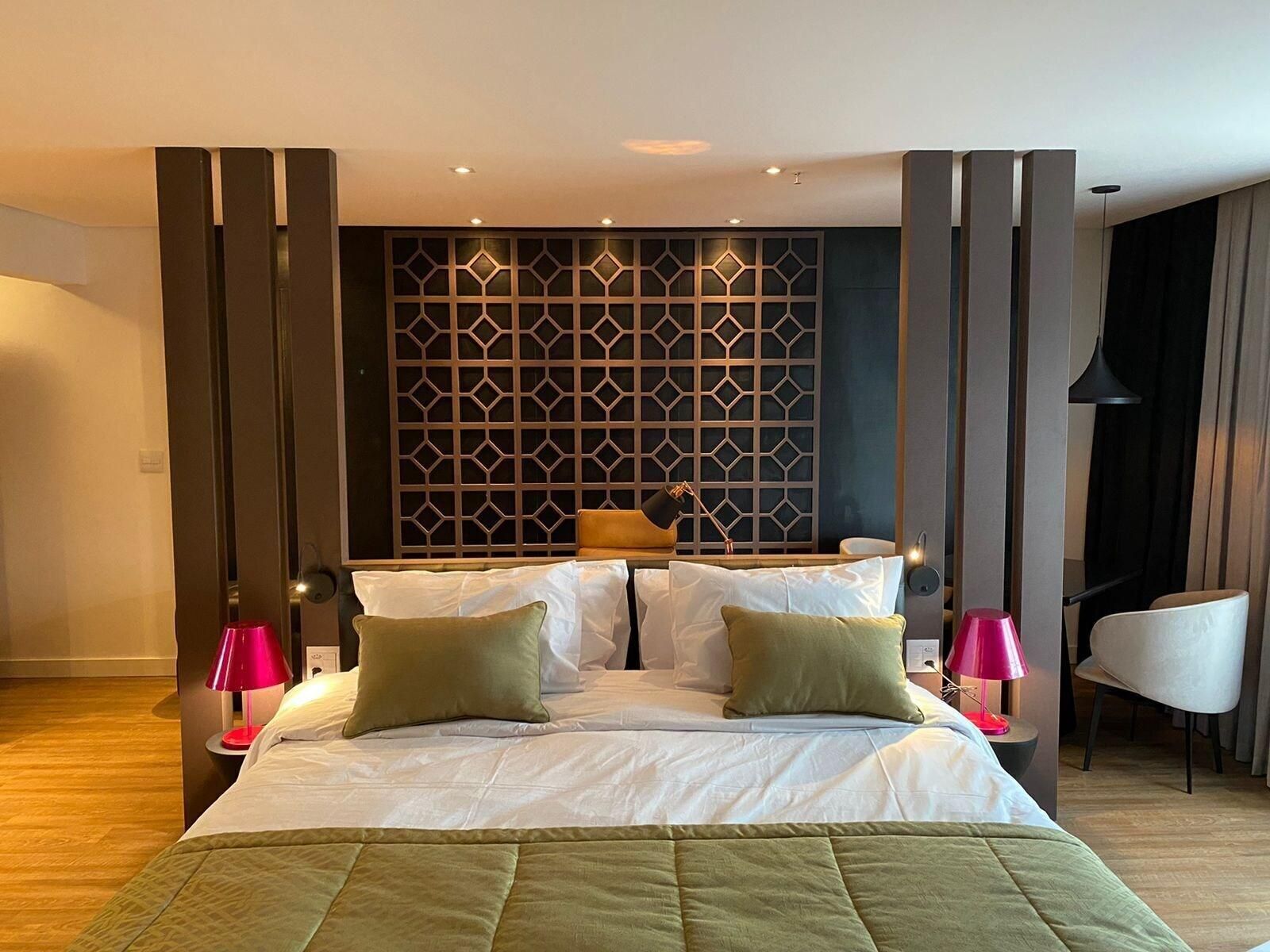 Habitación de hotel con una cama grande, dos mesitas de noche, un panel de pared moderno y una silla.