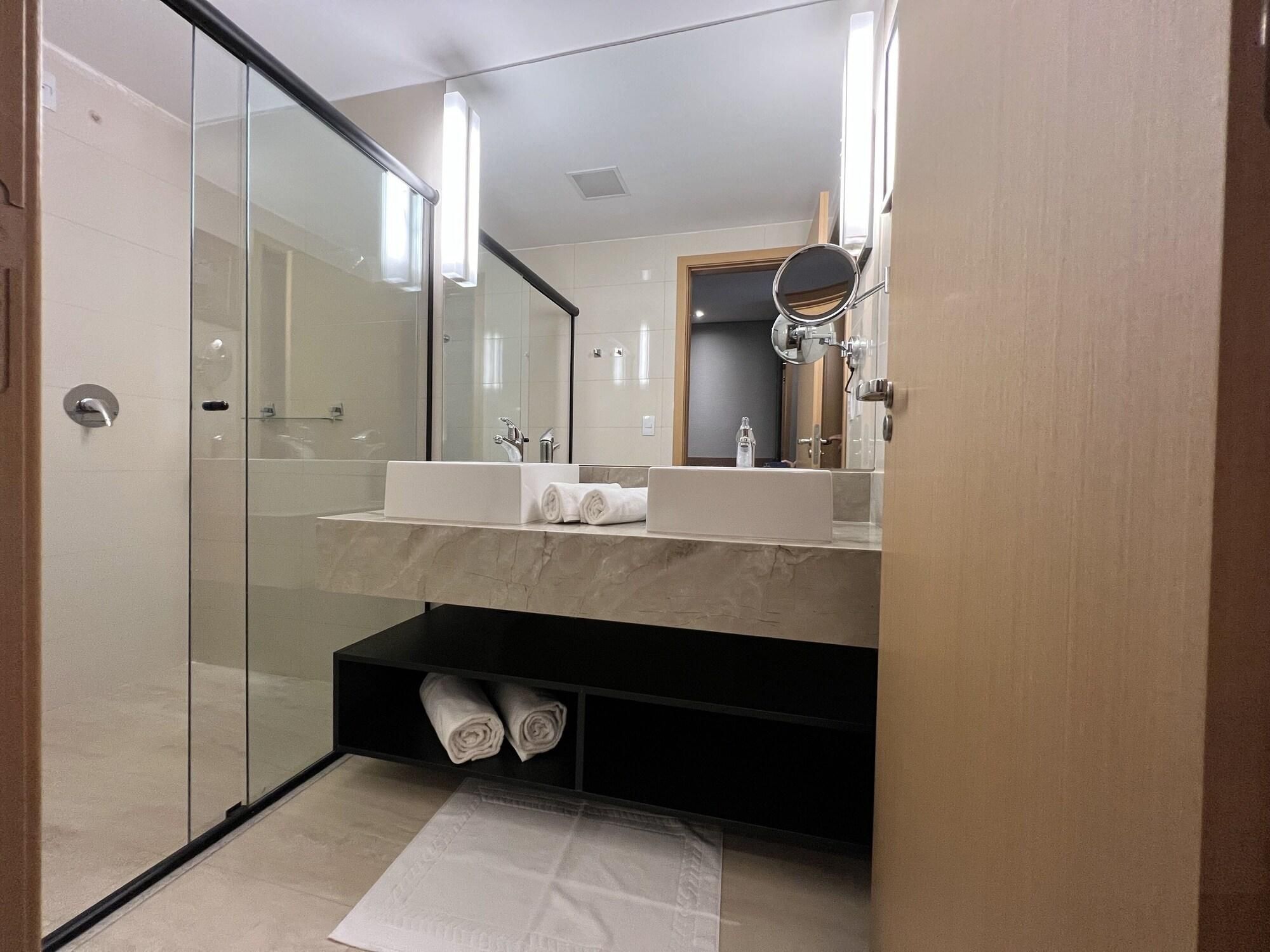 Un baño moderno con cabina de ducha de vidrio, tocador con lavabo y espejo, y un perchero para toallas.