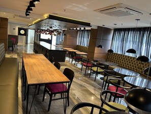 Een modern restaurant met een lange houten tafel, comfortabele zittingen en hanglampen.