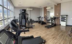 Un gimnasio con máquinas de cardio, equipo de pesas y una cinta de correr.