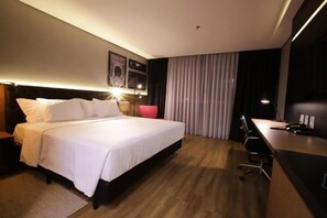 A modern hotel room with a large bed, a desk, and a chair. - Qs Marista Stay and Hotel (Goiânia)
