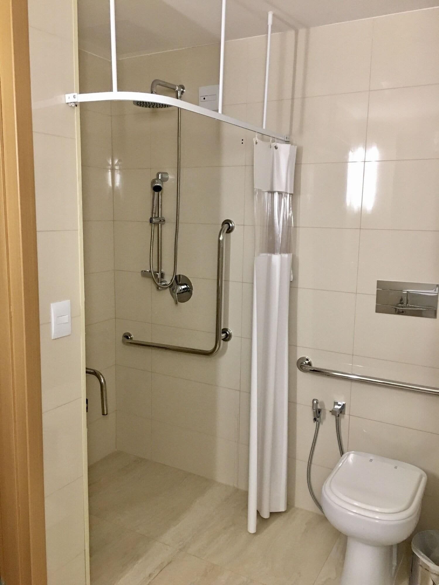 Un baño con ducha, inodoro y barras de apoyo.