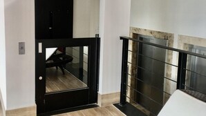 Una habitación moderna con una puerta de marco negro, un pequeño rincón de descanso y vistas a un balcón con barandilla metálica.