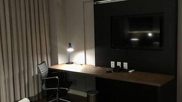 Una habitación de hotel moderna con una cama grande, un escritorio con computadora, una silla, un televisor montado en la pared y una lámpara.
