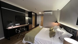 Una habitación de hotel moderna con una cama grande, un escritorio, una silla, un televisor y un equipo de aire acondicionado.