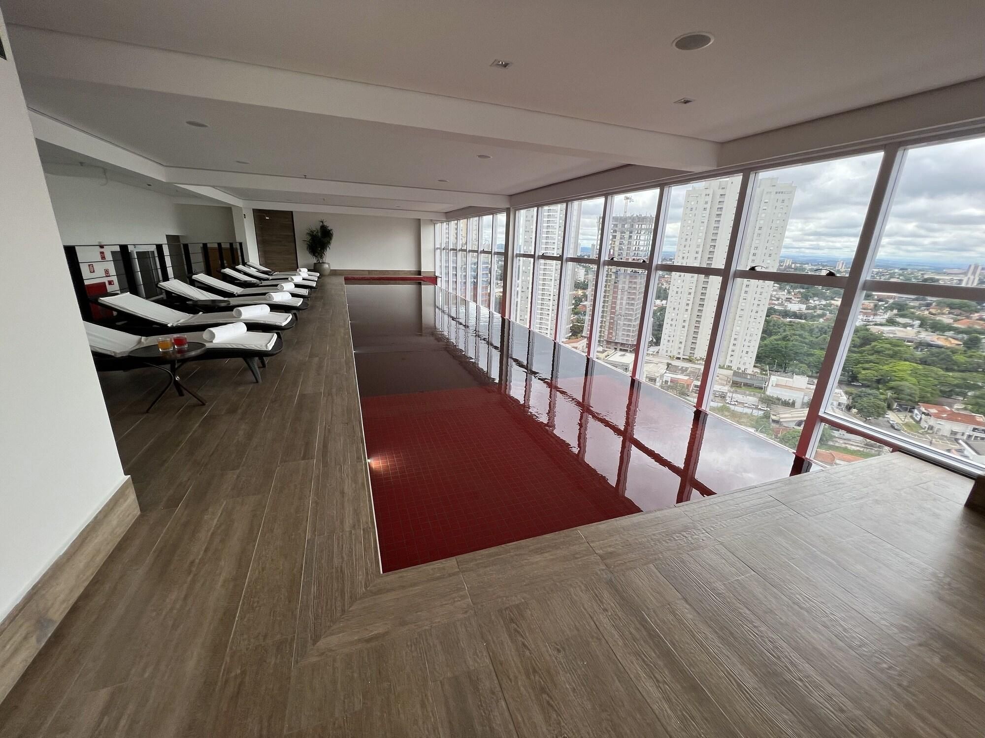 Habitación de hotel moderna con distribución alargada, alfombra roja y una fila de sillones de masaje. Amplias ventanas ofrecen vistas a la ciudad.