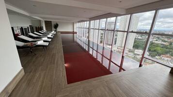 Habitación de hotel moderna con distribución alargada, alfombra roja y una fila de sillones de masaje. Amplias ventanas ofrecen vistas a la ciudad.