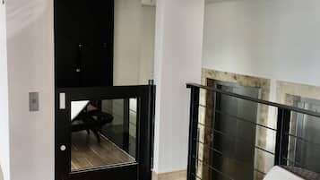 Una habitación moderna con una puerta de marco negro, un pequeño rincón de descanso y vistas a un balcón con barandilla metálica.