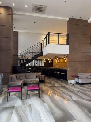 Ein großzügiger Wohnbereich mit moderner Treppe, einer Sitzecke mit Sofa und Hocker sowie einer Bar mit Hockern.