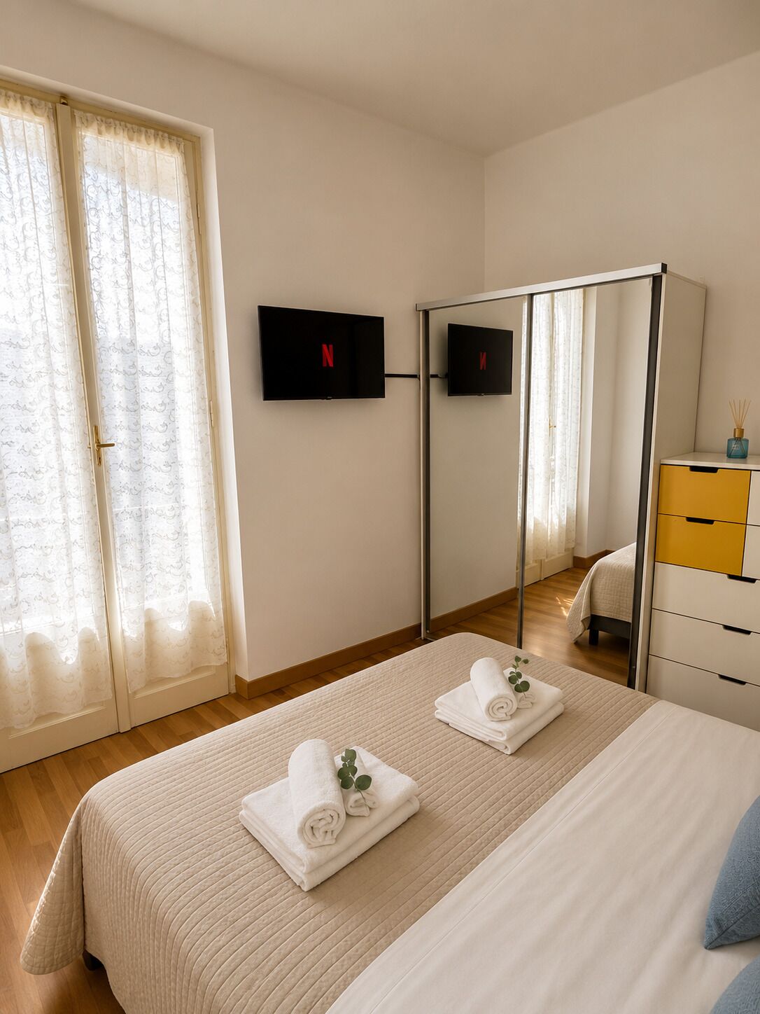 A bedroom with a bed, a wardrobe, a TV, and a window with curtains.