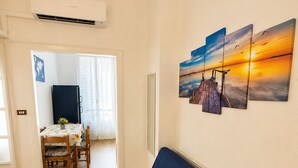 Un soggiorno con divano blu, pavimento in legno, angolo da pranzo con tavolo e sedie, e condizionatore d'aria a parete.