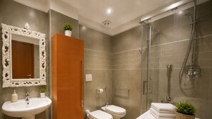 Moderni kylpyhuone, jossa on pesuallas, peili, wc, suihku ja kaappi.