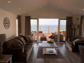 Un amplio salón con grandes ventanales con vistas al mar, amueblado con sofás y una mesa de centro.