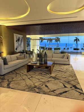 A modern living room with a large window overlooking a pool and palm trees, a large abstract painting, and a patterned rug. - 4 BR Luxury oceanfront corner residence at Tres Mares in Marina Vallarta PV (Puerto Vallarta)