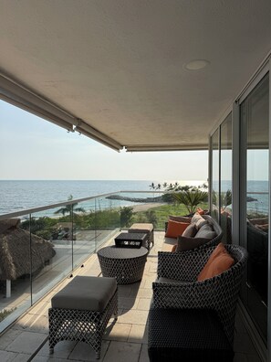 A balcony with wicker furniture, a glass railing, and a view of the sea. - 4 BR Luxury oceanfront corner residence at Tres Mares in Marina Vallarta PV (Puerto Vallarta)