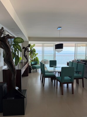 A modern living room with a dining area, large windows, and a view of the sea. - 4 BR Luxury oceanfront corner residence at Tres Mares in Marina Vallarta PV (Puerto Vallarta)