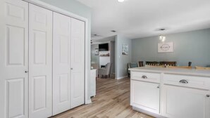 A kitchen with white cabinets, a wooden countertop, and a dining area with a table and chairs. - Coastal Home with Outdoor Oasis. Golf Cart Avail (Long Beach)