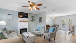 A spacious living room with a fireplace, two armchairs, a coffee table, and a ceiling fan. - Coastal Home with Outdoor Oasis. Golf Cart Avail (Long Beach)