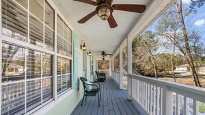 A covered porch with a ceiling fan, large windows, and outdoor seating. - Coastal Home with Outdoor Oasis. Golf Cart Avail (Long Beach)