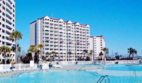 Un hotel con varios balcones, piscina y palmeras.