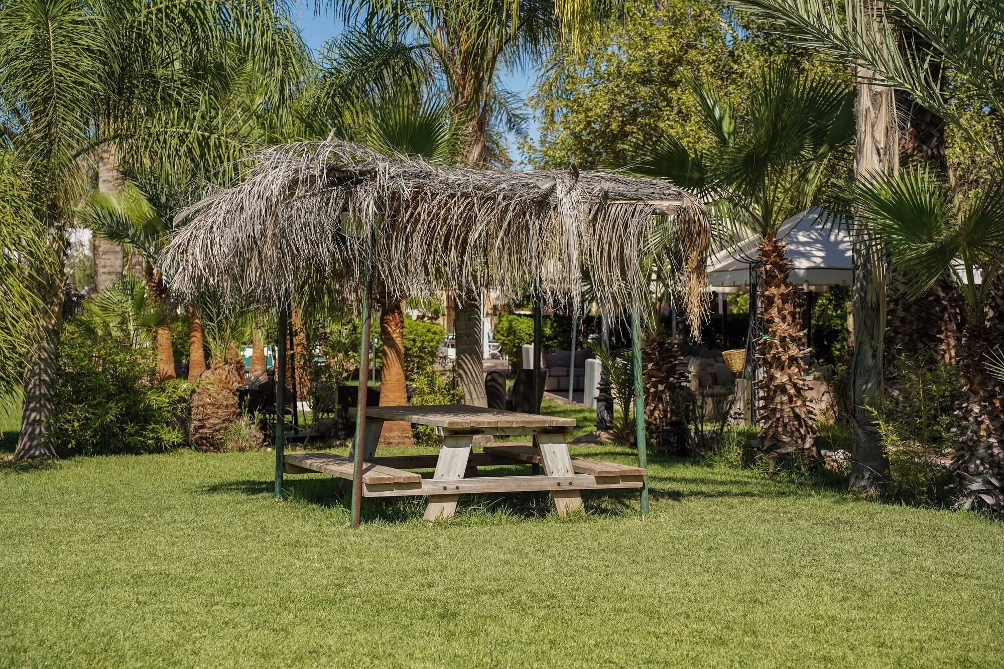 A wooden gazebo with a thatched roof in a lush garden setting.