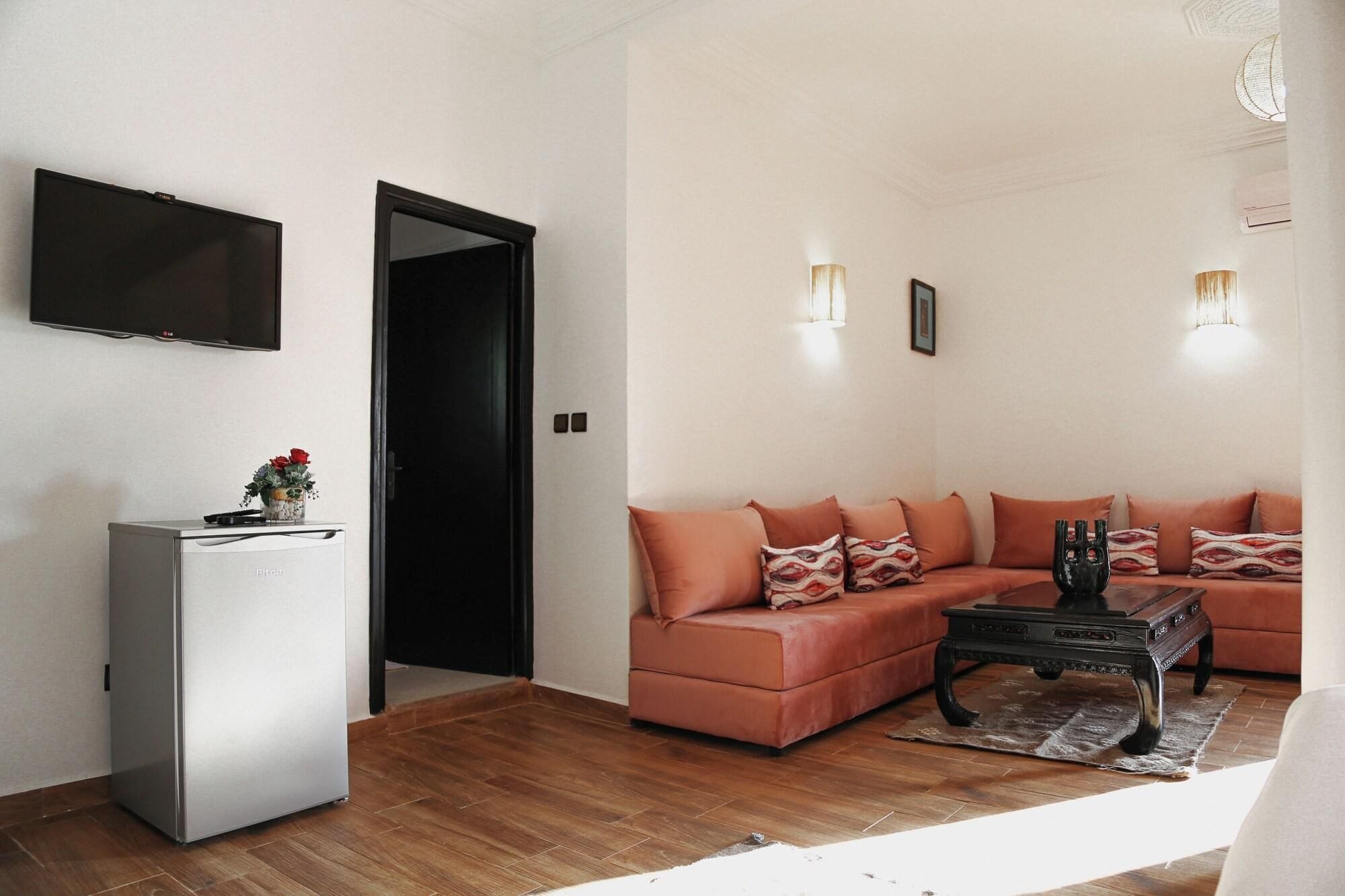 A living room with a sectional sofa, a flat-screen TV, a refrigerator, and a door leading to another room.