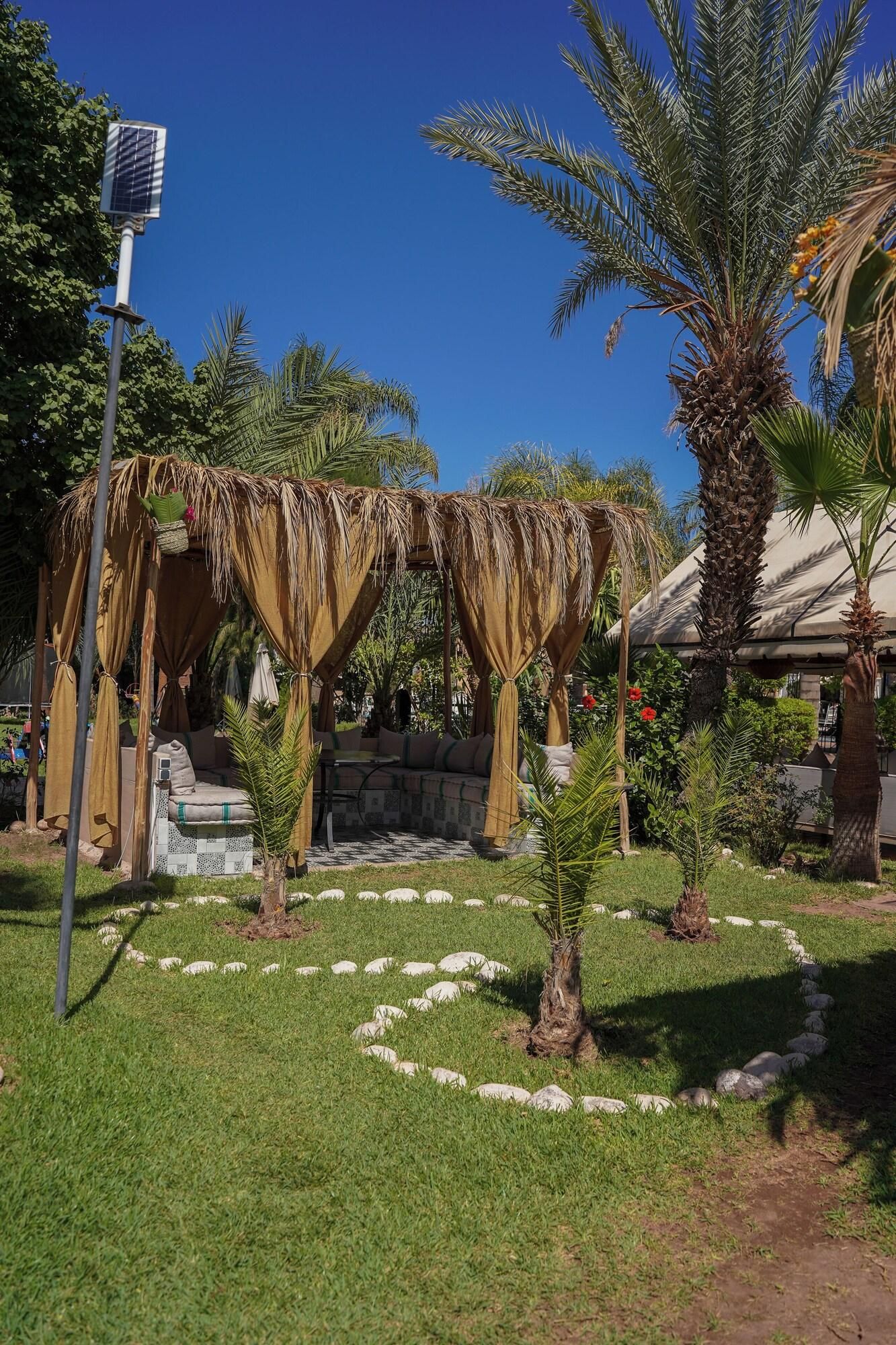 A garden with a thatched gazebo, a palm tree, and a solar panel.