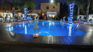 A swimming pool with a wooden deck, surrounded by palm trees and outdoor seating.