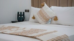Ein ordentlich bezogenes Bett mit gemusterten Textilien, einem dekorativen Kissen und einem kleinen Nachttisch mit einer Vase.